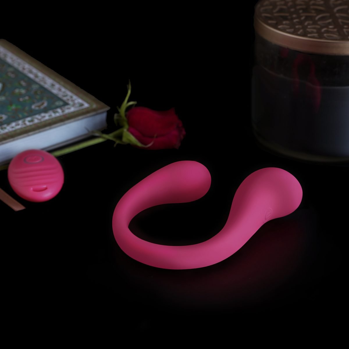 The Erotx Omni Duet bendable vibrator in magenta with its remote, on a dark table beside a rose